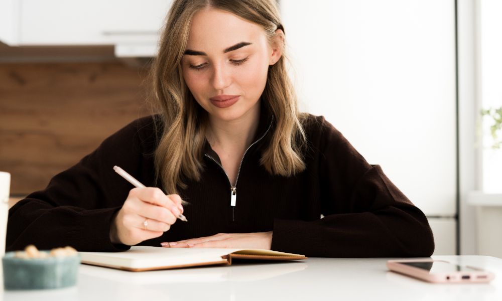 A young woman writing in a journal at a table.