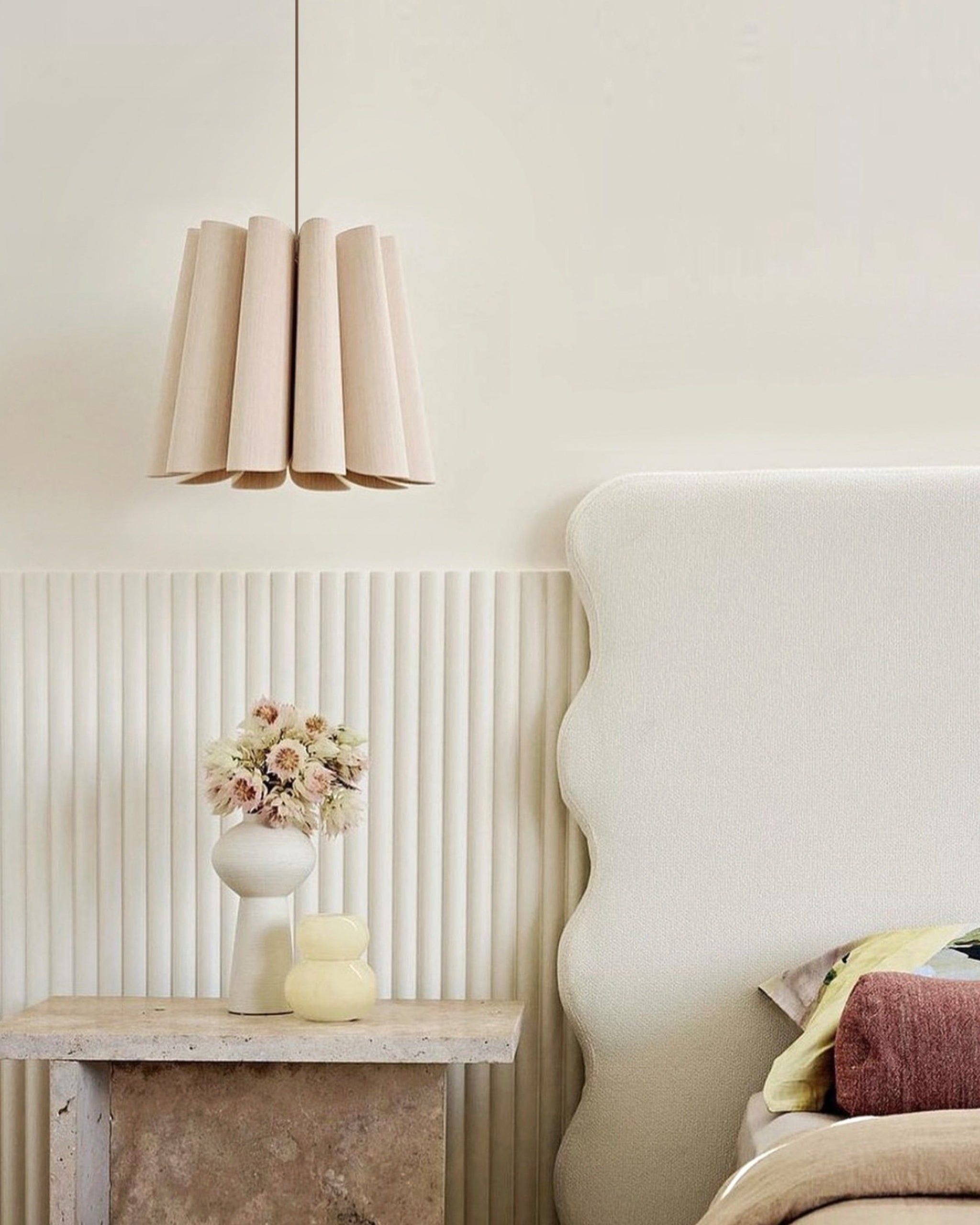 Decorative lampshade hanging above a table with a vase and flowers against a neutral wall.