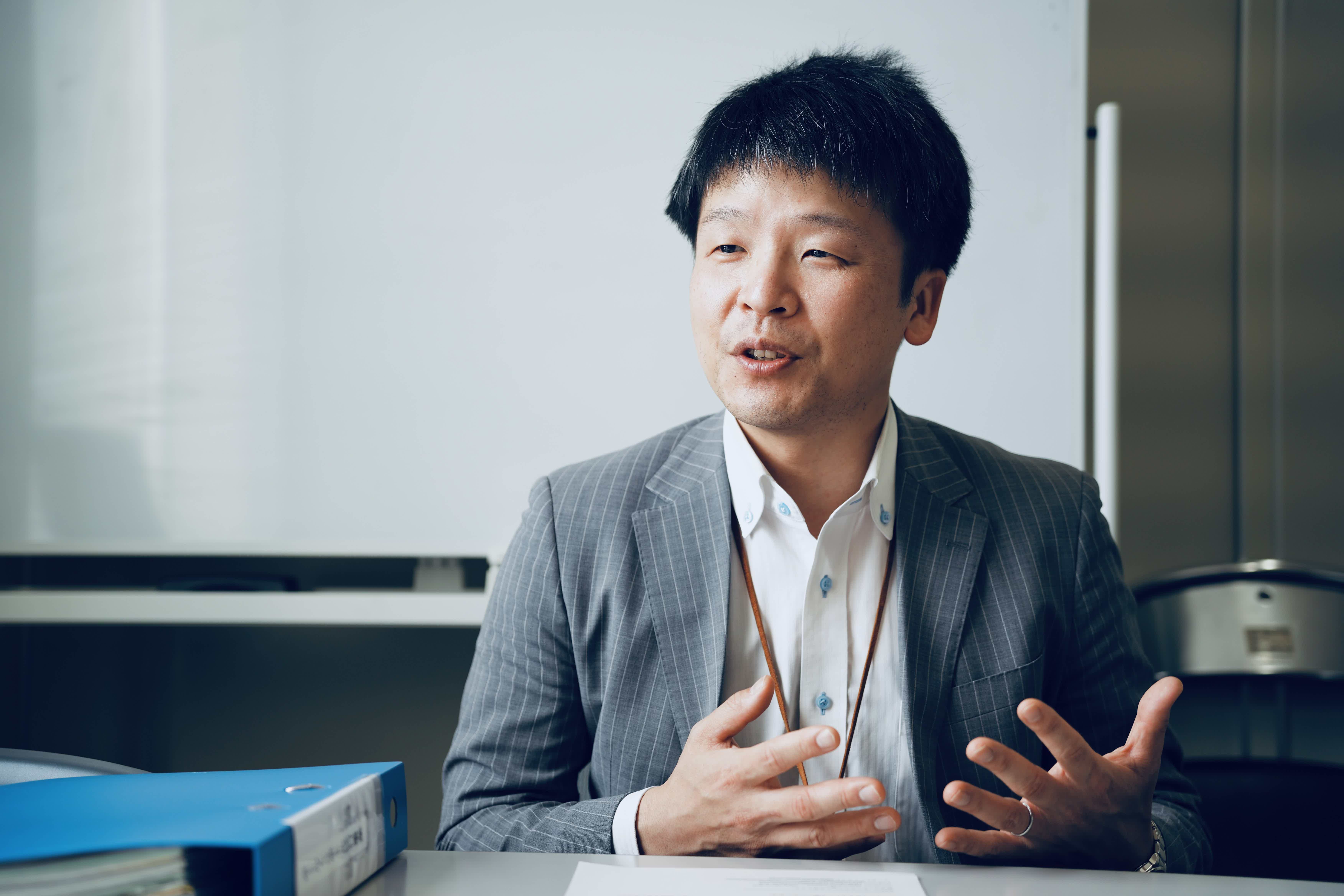A man in a suit speaking in an office setting.