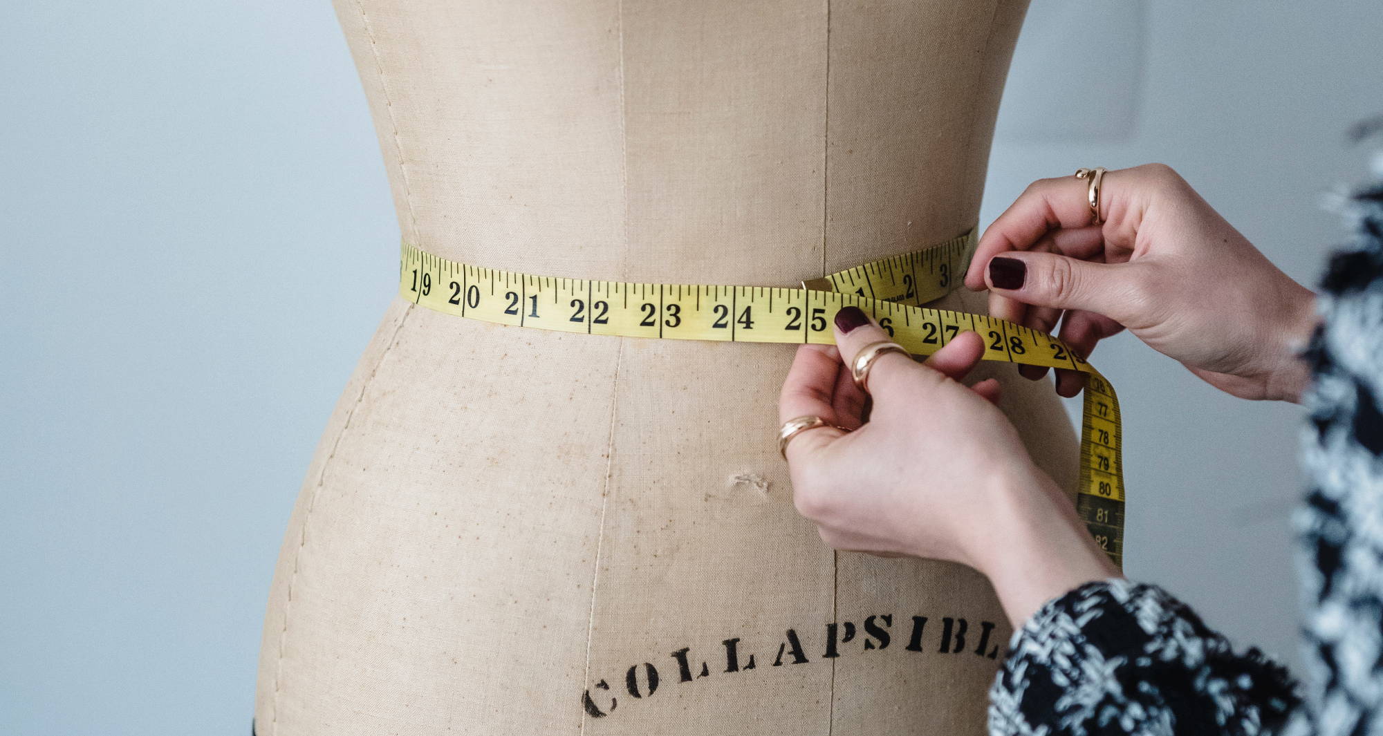 A woman  measures the waist of a beige mannequin
