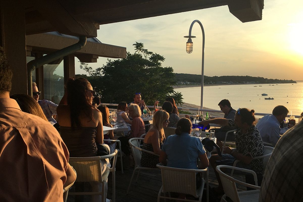 People dining outdoors at sunset by the water.