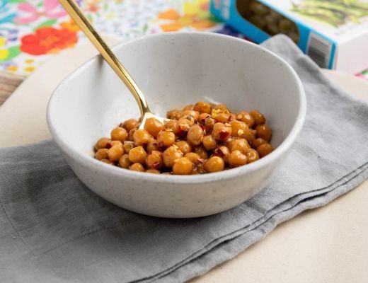 Bowl of chickpeas with a gold spoon on a linen napkin.
