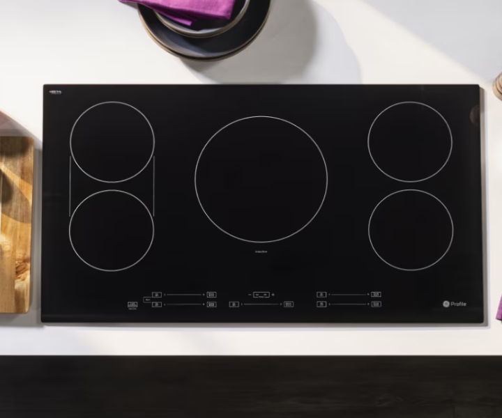 Black induction cooktop with four circular burners on a countertop.