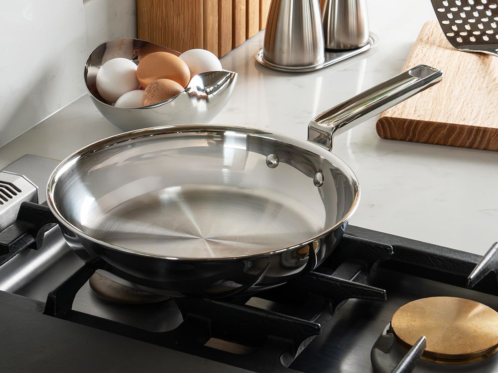 316 Series stainless-steel frying pan on a gas stove beside eggs and utensils.