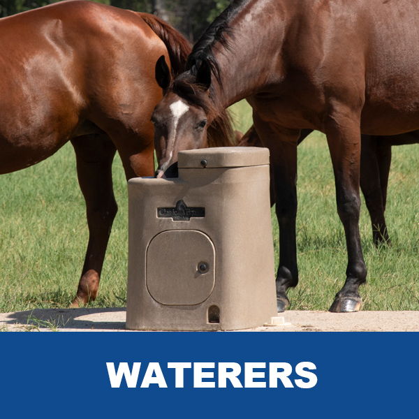 Two horses drinking from a water trough in a green field.