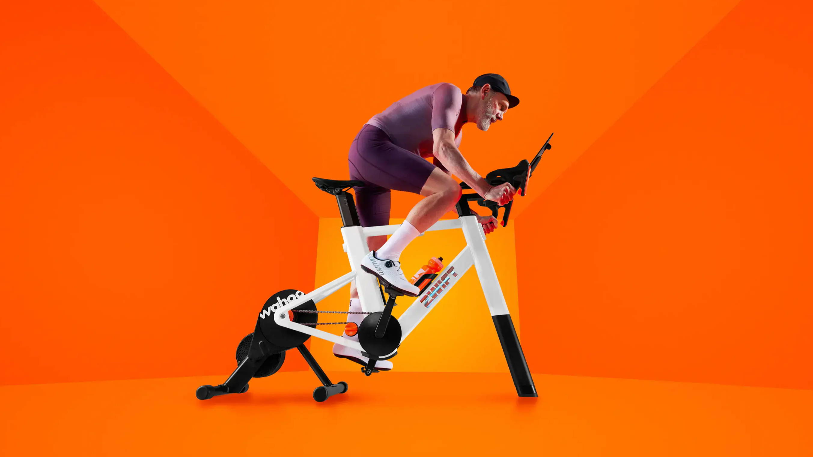 Athlet fährt auf einem Zwift-Indoor-Bike mit Smart-Trainer in aerodynamischer Position, vor leuchtend orangem, minimalistischen Hintergrund.