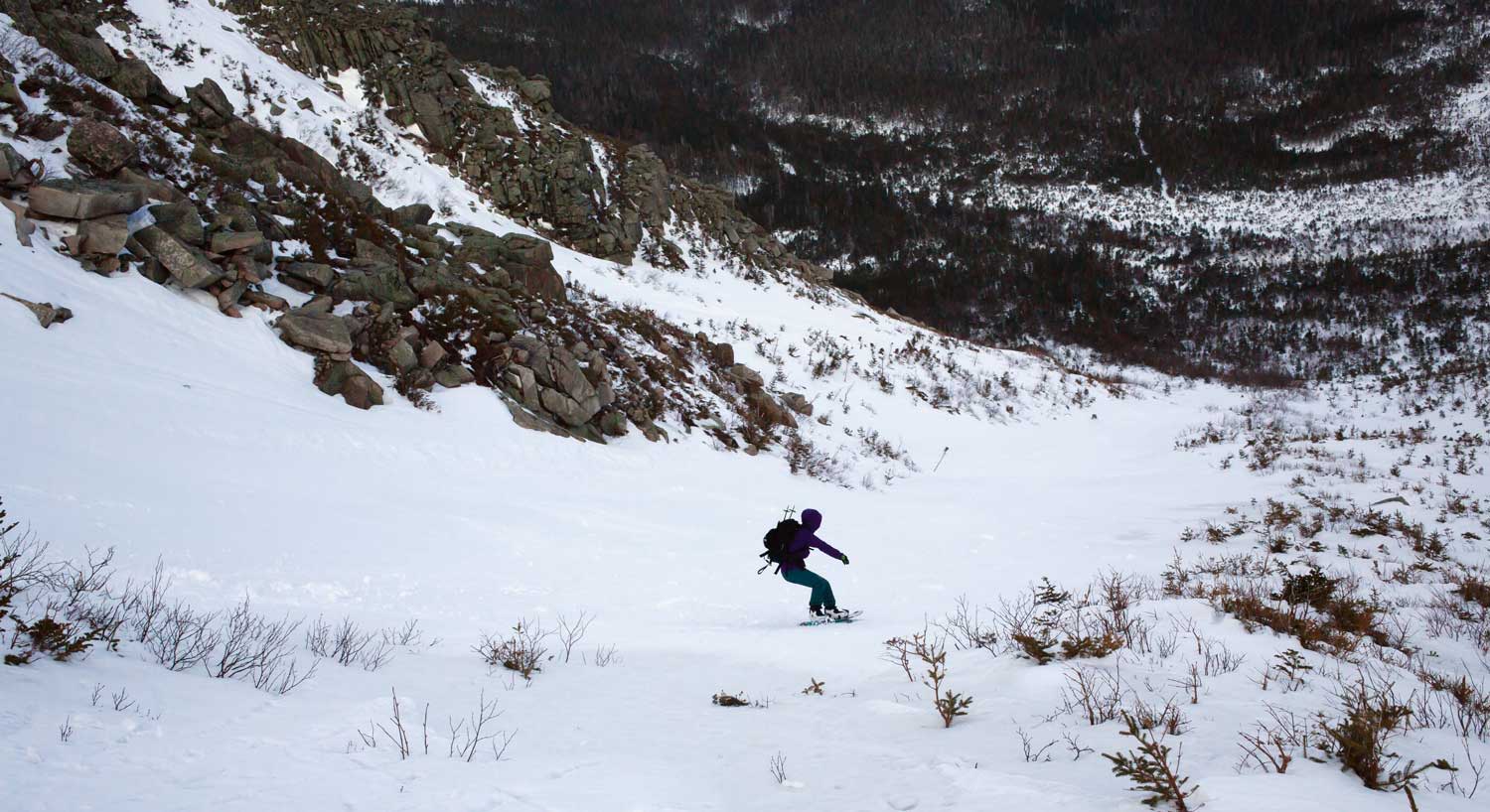 A person snowboarding down a snowy slope in a mountainous area.