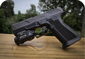 A handgun with a tactical light on a wooden surface outdoors.
