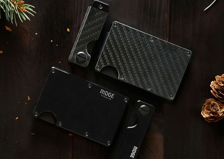 Various sleek black wallets on a wooden surface with pinecones.