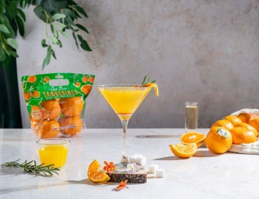 A cocktail and oranges on a table with green packaging in the background.