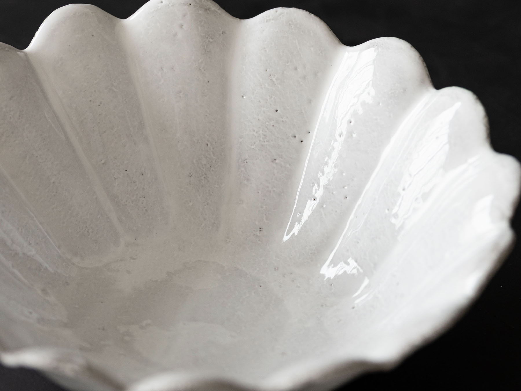 A white, scalloped ceramic bowl on a dark background.