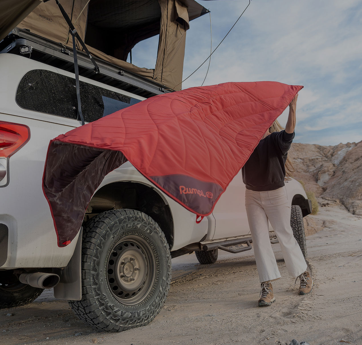 Person setting up a red camping ground mat next to a white truck.