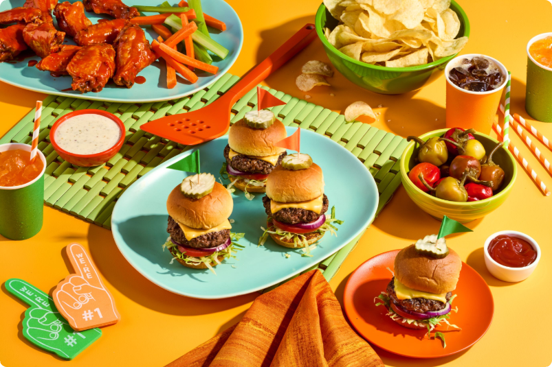 A colorful spread of sliders, wings, chips, and drinks on a vibrant table.