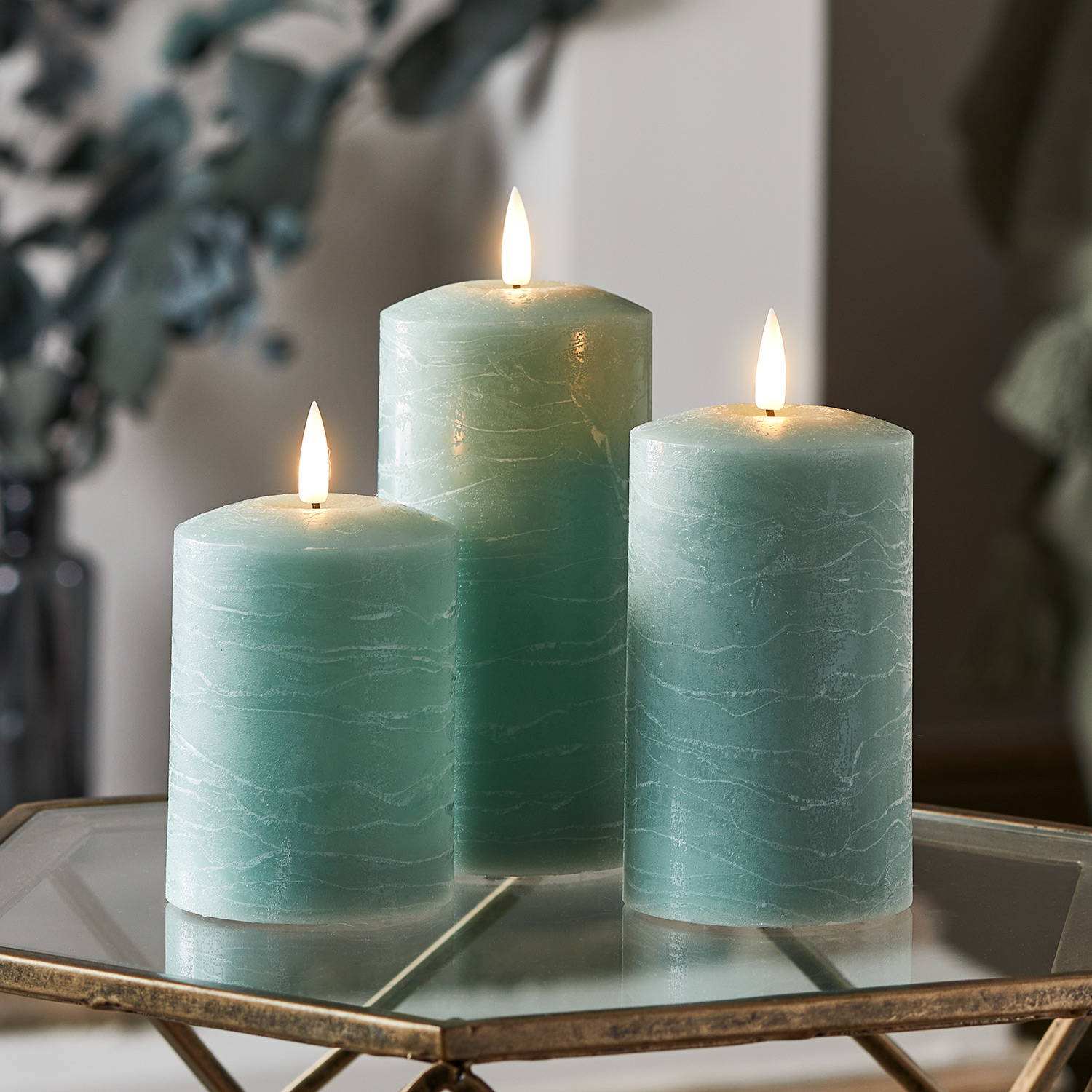 3 green LED pillar candles on a glass side table in a living room.