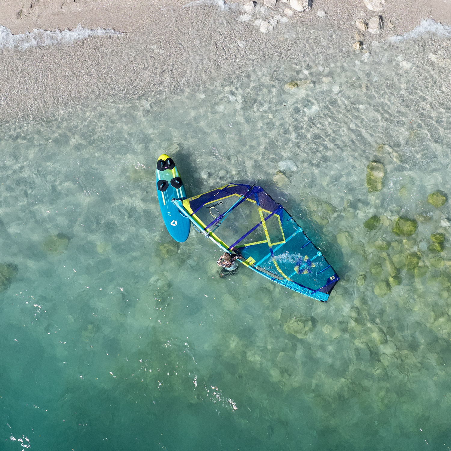 Aerial view of a windsurfing board near a sandy beach.