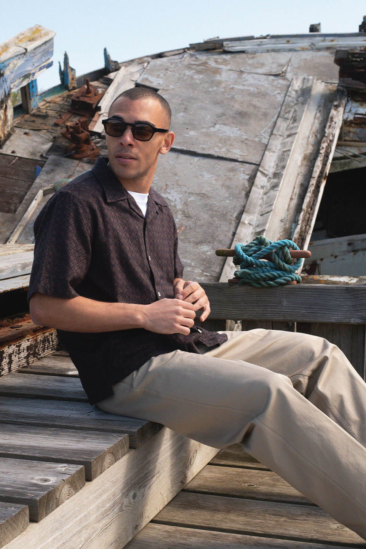 Man sitting on a dock, wearing sunglasses and casual clothing.