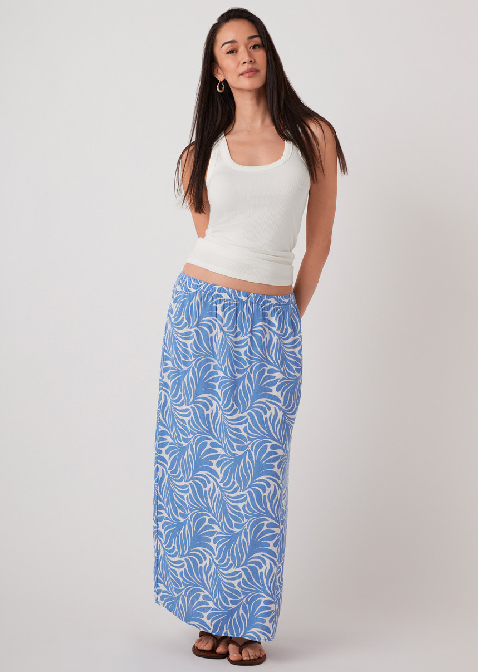 Woman wearing a white tank top and blue patterned maxi skirt.