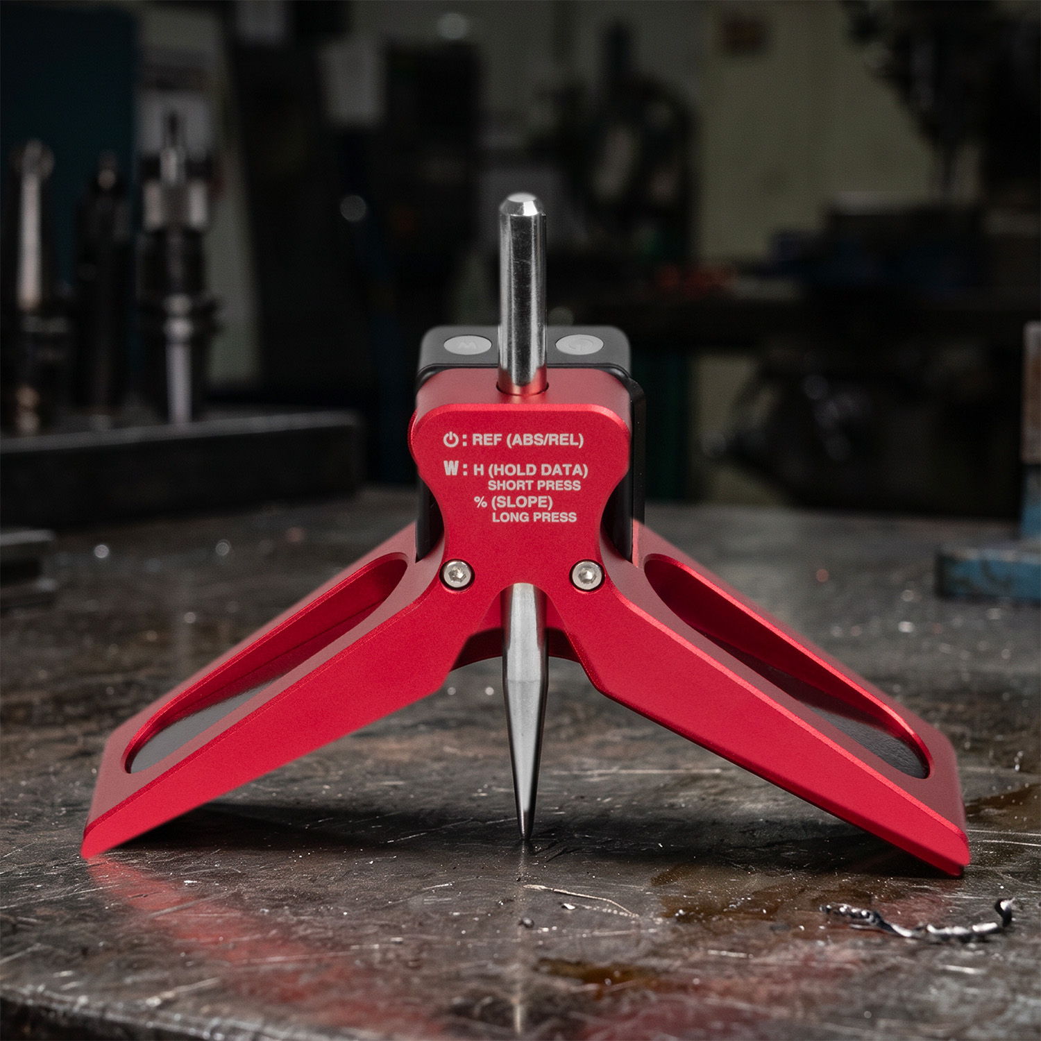 Red mechanical tool with a pointed tip and tripod base on a workbench.