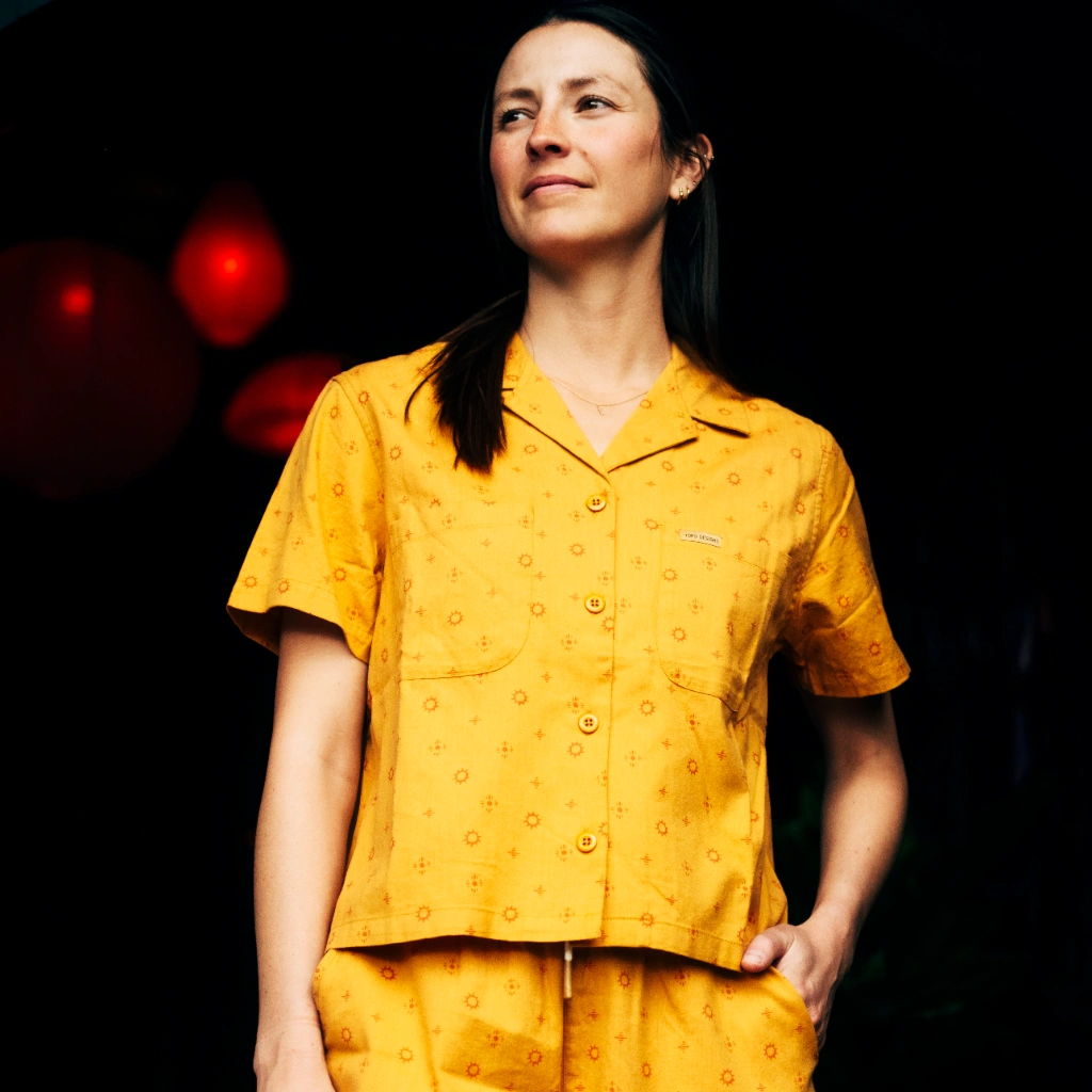 Woman in yellow pajamas standing confidently against a dark background.