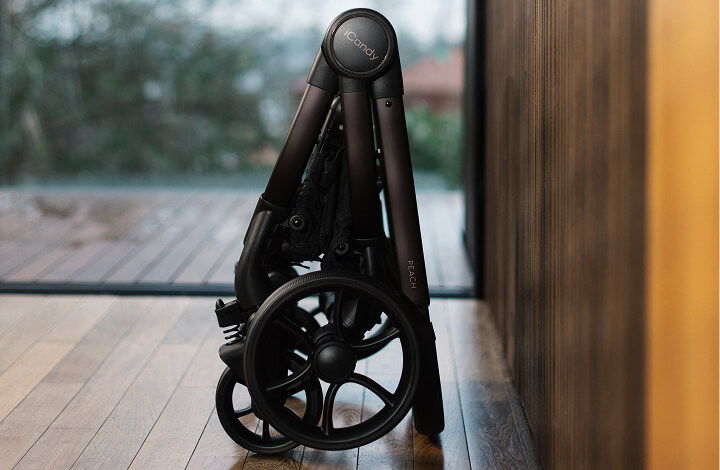 Folding iCandy Peach 8 stroller leaning against a wooden wall indoors.