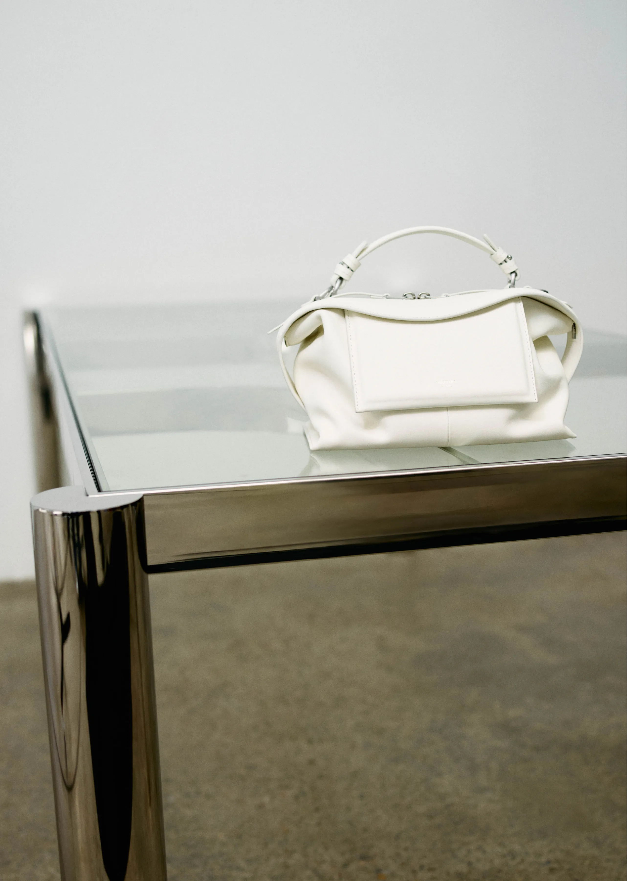 A white handbag placed on a modern glass and metal table.