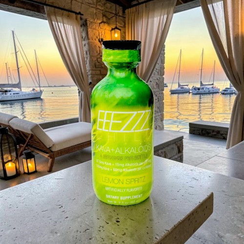 Green bottle on a table with a sunset and boats in the background.