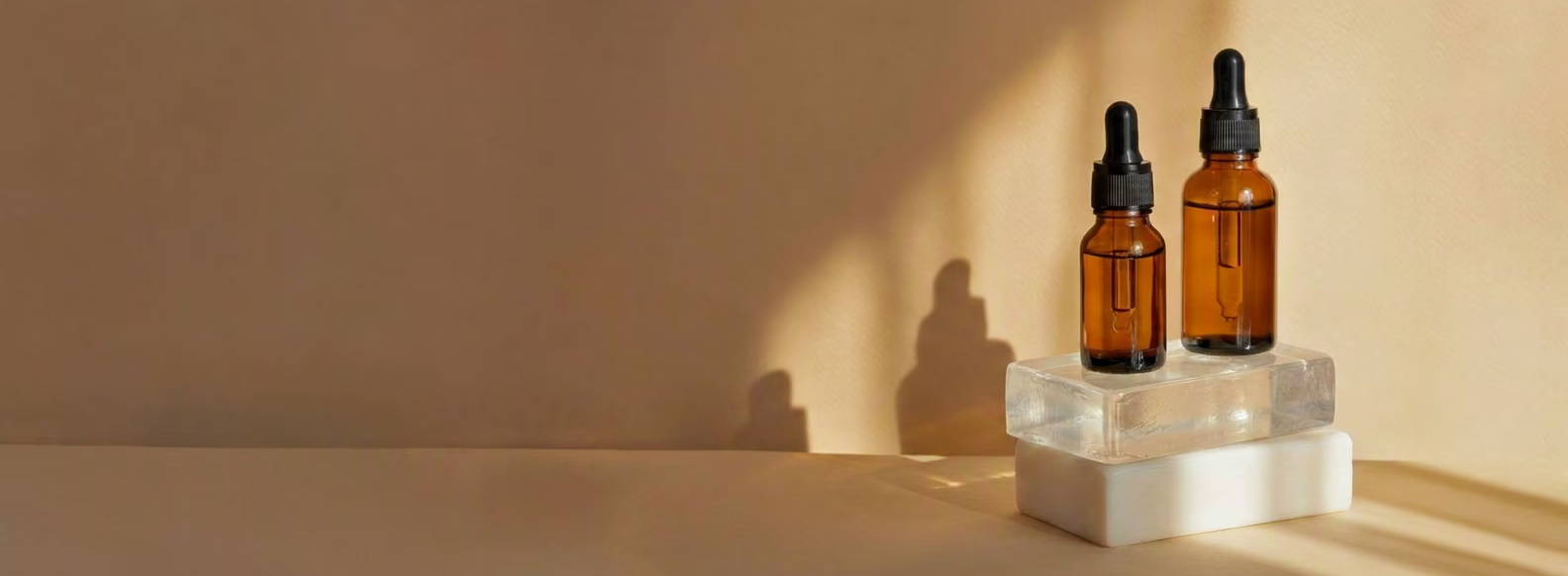 Two amber glass bottles on a white pedestal with soft shadows.