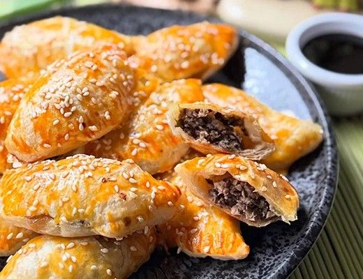 Plate of golden pastries with sesame seeds and a dipping sauce.