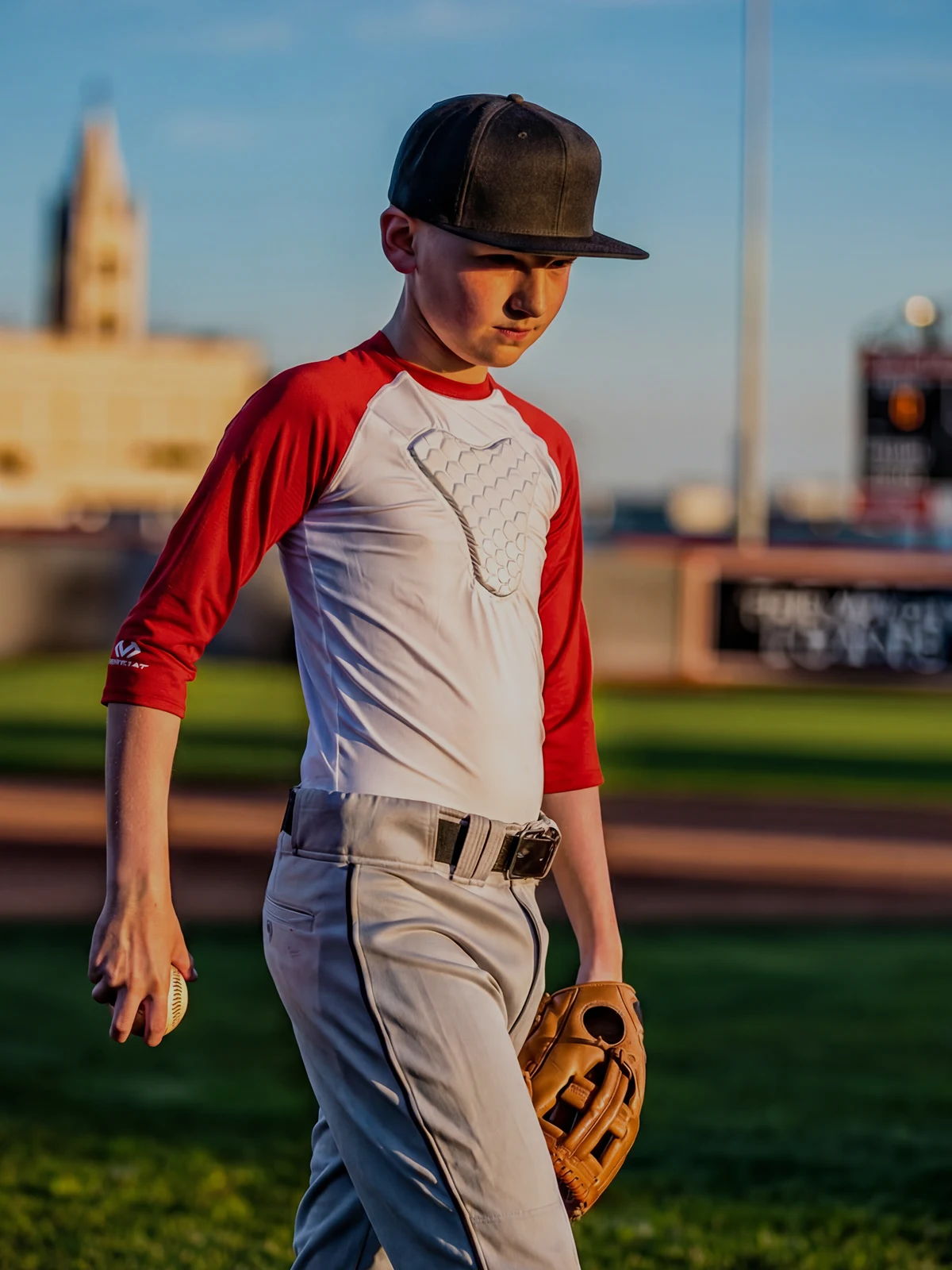 A young baseball player walking on the field, wearing a cap and glove.
