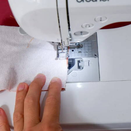 Sewing a seam with a sewing machine, you see a hand and fabric piece and orange thread
