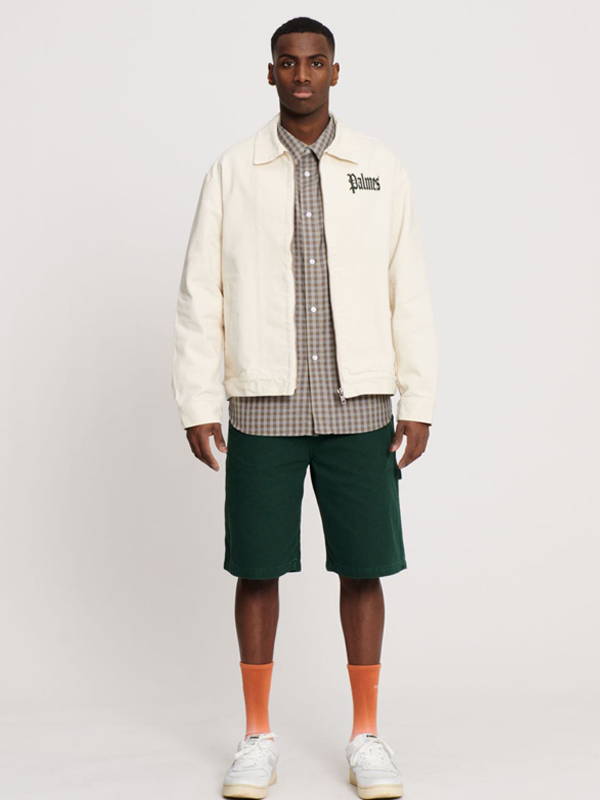A model wearing the Palmes Olde Zip Jacket in Off White with a check shirt and shorts.