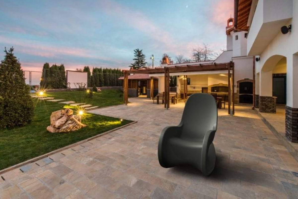 A sleek grey all-weather rocking chair on a cobblestone patio at dusk.