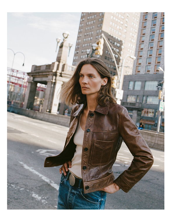 A person in a brown jacket poses on a city street.