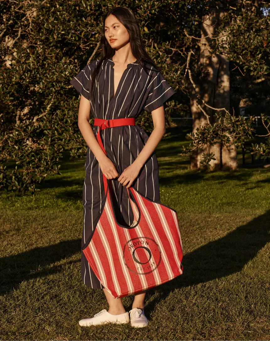 Woman in a striped dress holding a large striped bag outdoors.