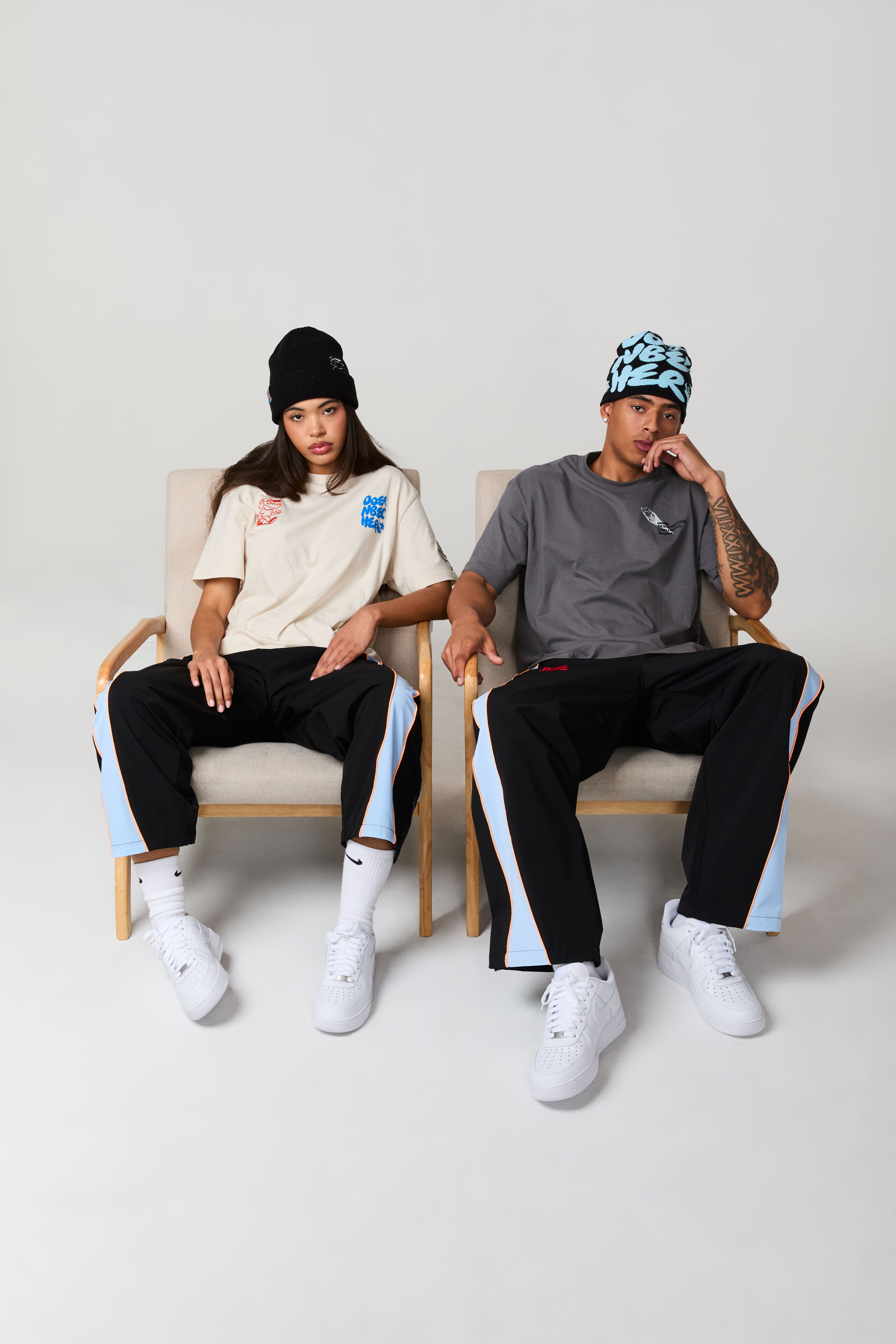 Two people in casual outfits sitting on chairs against a plain background.