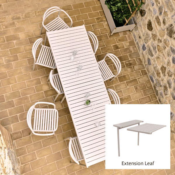 White outdoor extension dining table with matching chairs and extension leaf detail in a stone courtyard.