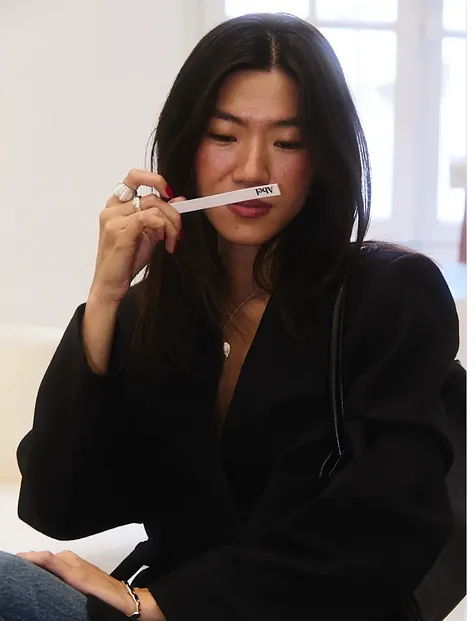 Woman holding a white object near her mouth, wearing a black jacket.