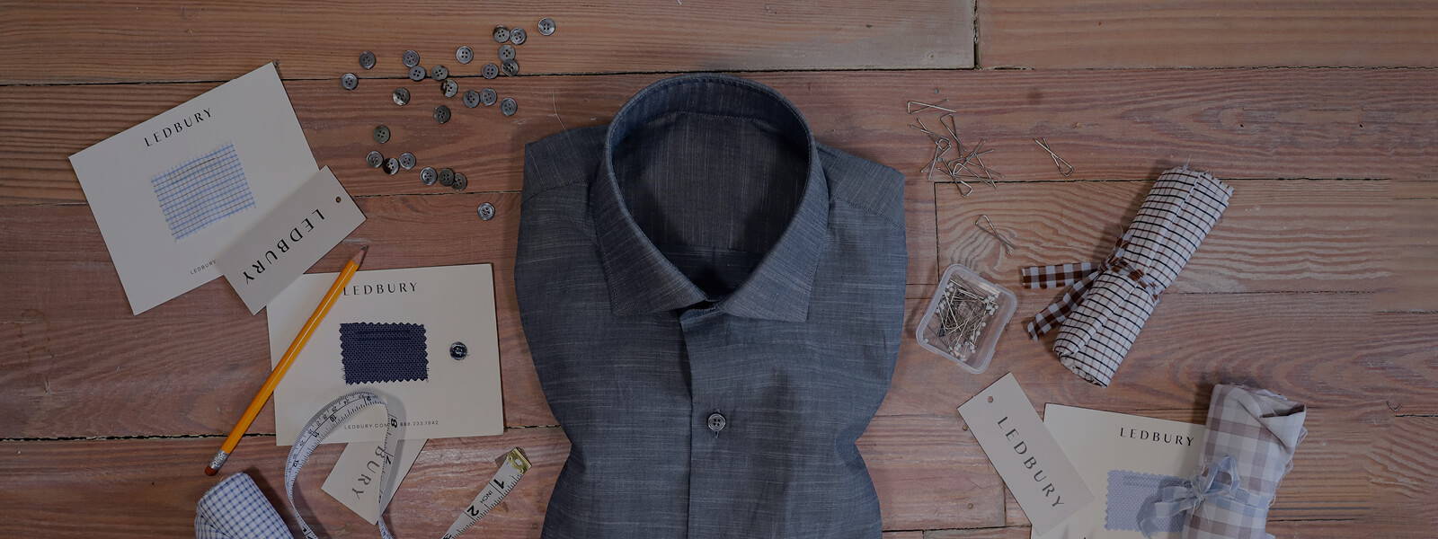 Men's slate blue chambray dress shirt folded against a wooden background