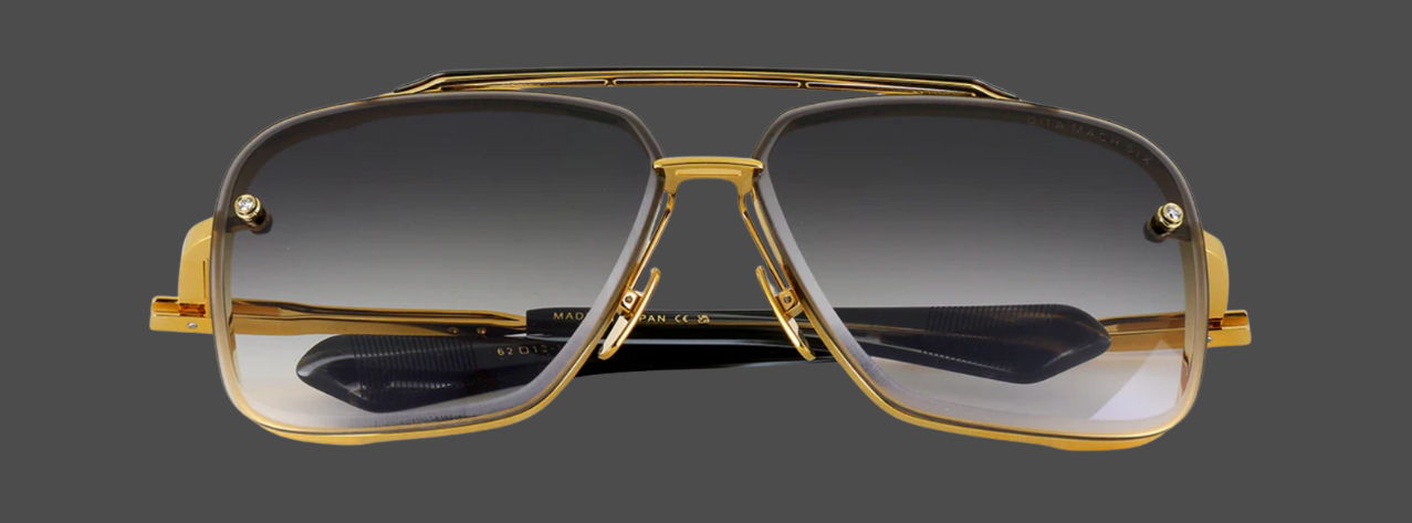 Gold-framed sunglasses with gradient dark lenses on a gray background.