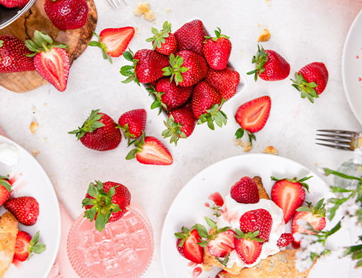 A spread of strawberries on plates and a table, with a drink.