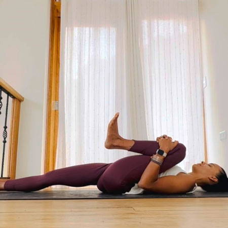 Chelsea in third yoga pose, on back with left leg to chest and right leg extended out..