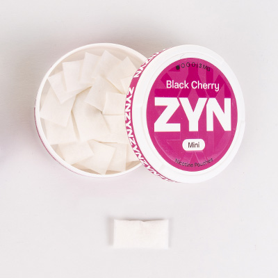 Container of ZYN Black Cherry nicotine pouches with one mini pouch outside.