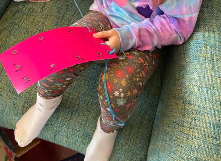 child lacing blue yarn through bright pink lacing card
