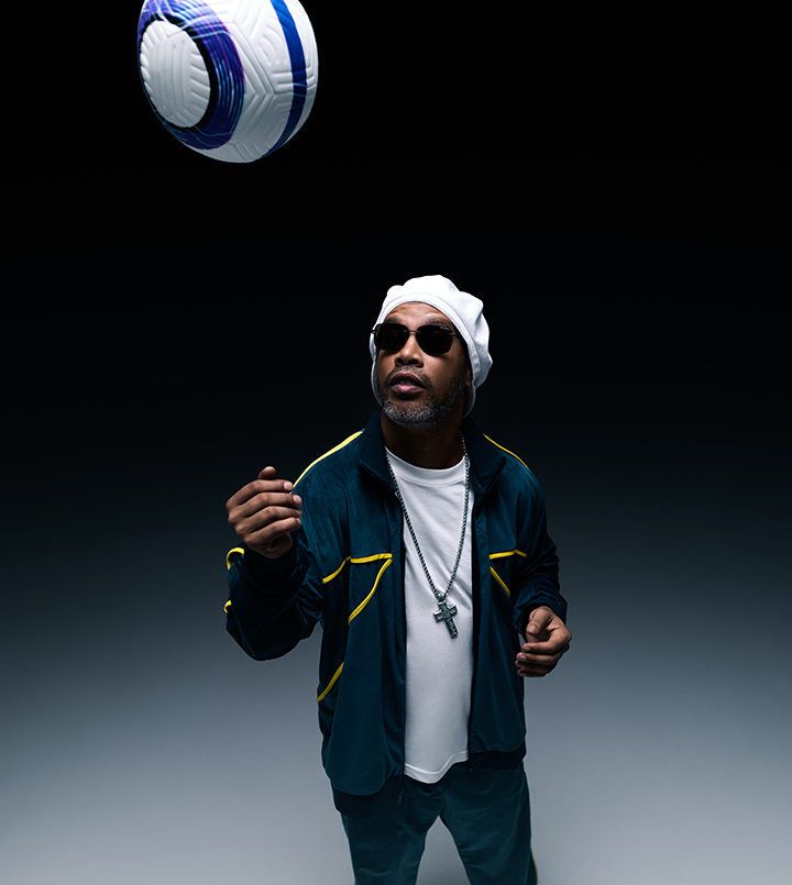 Person in a hat and sunglasses watching a soccer ball in mid-air.