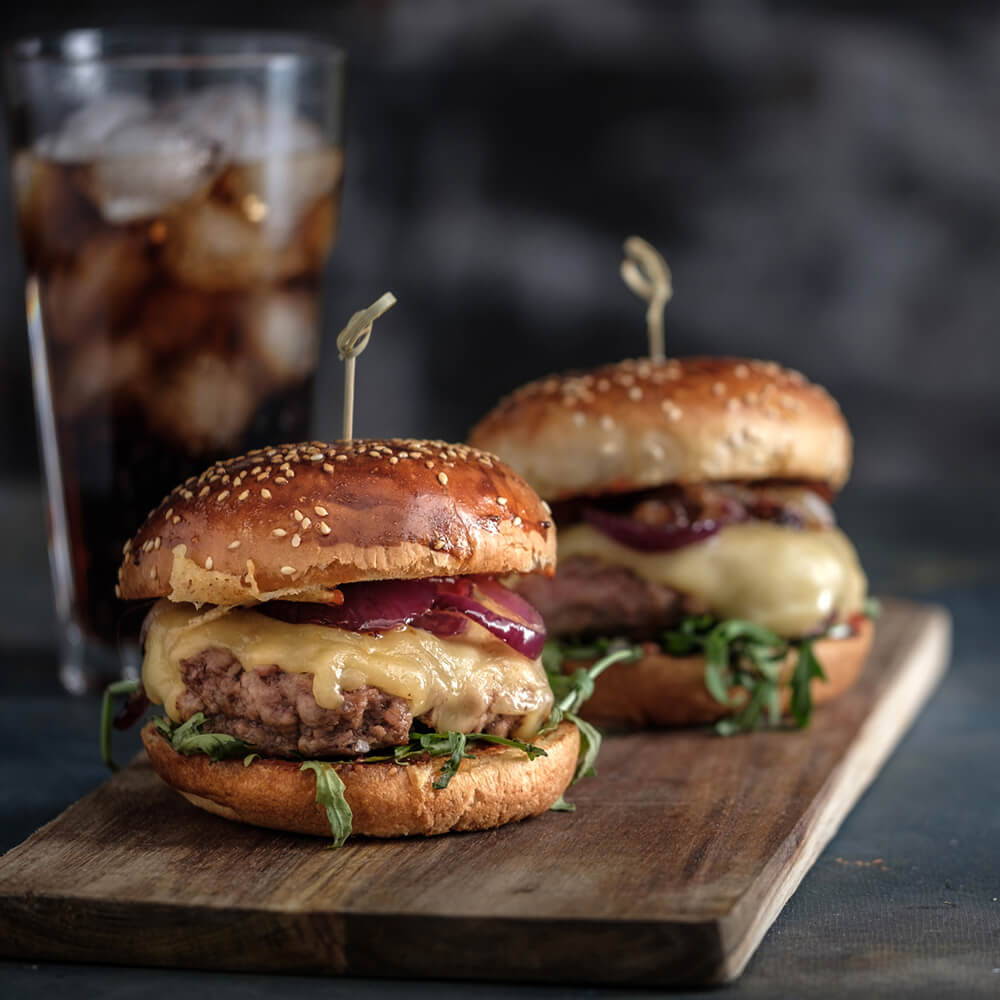 two burgers with melted cheese with a coke in the background