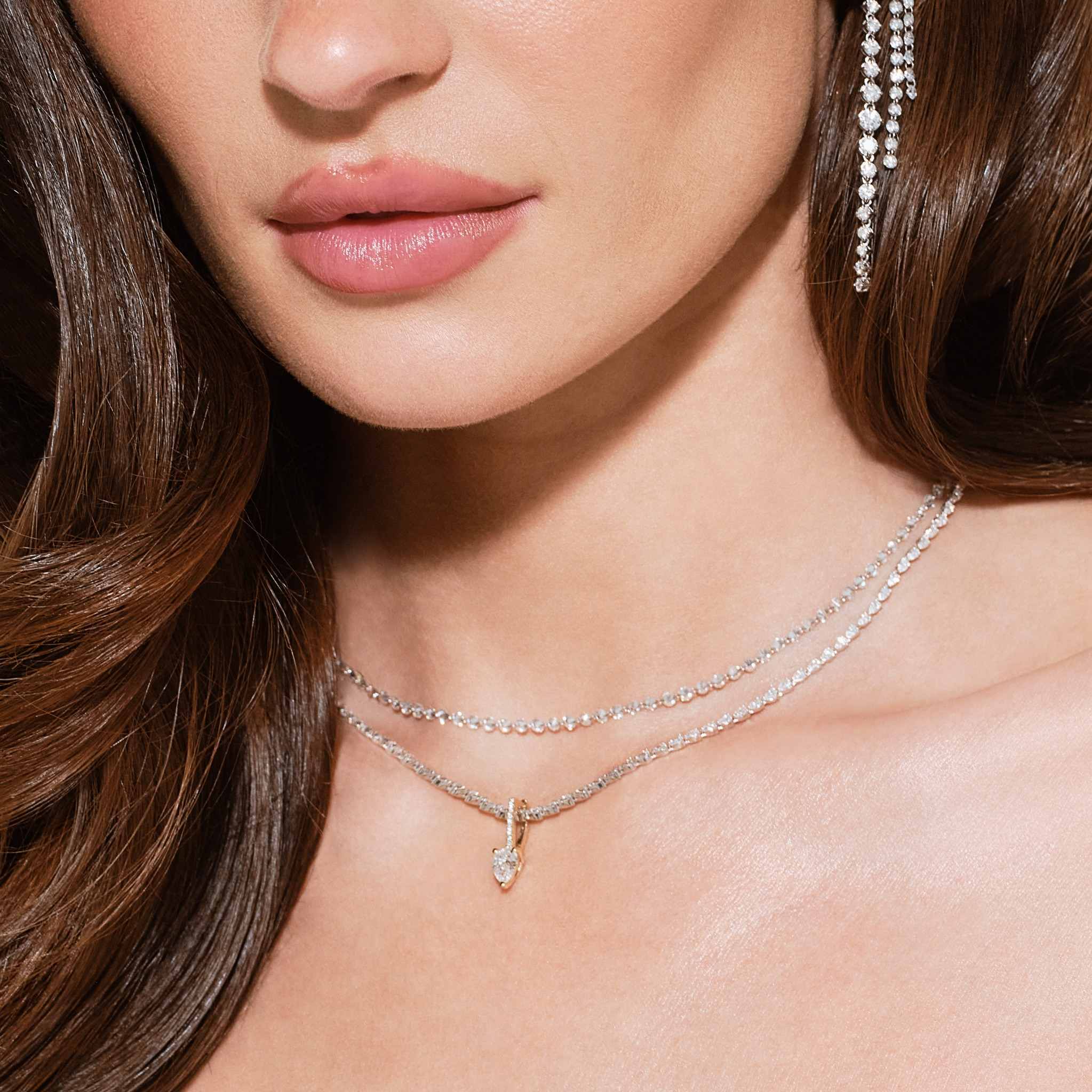 Close-up of a woman's neck adorned with layered necklaces and earrings.