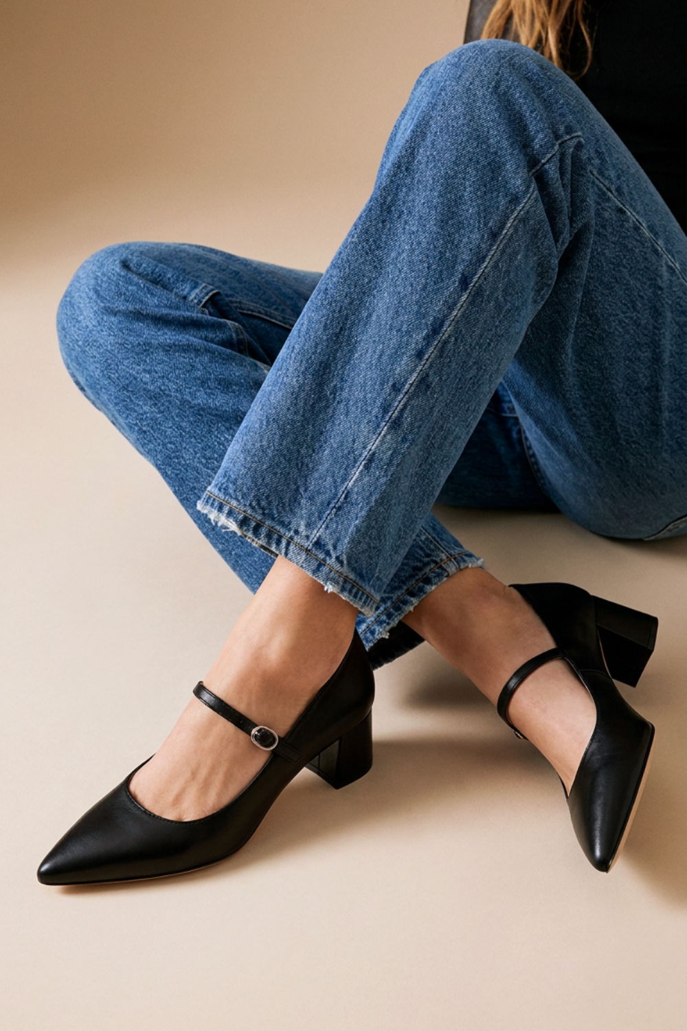 A person wearing black heeled shoes and blue jeans, seated against a neutral background.