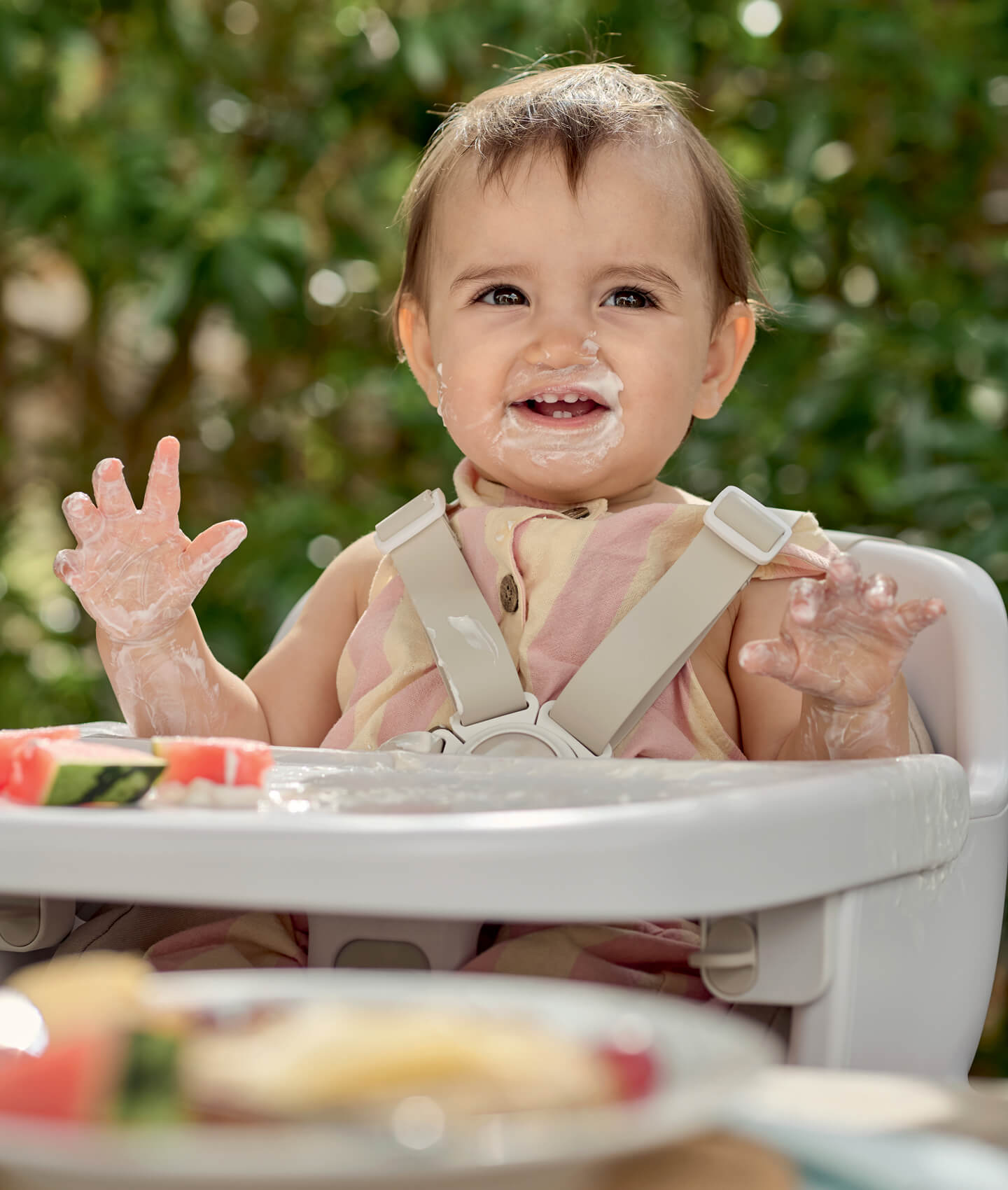 Baby in a high chair, smiling with food on their face.