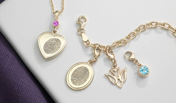 yellow gold heart shaped fingerprint necklace with a pink Swarovski birthstone bail and a yellow gold oval shaped fingerprint charm bracelet with a dove symbolic charm and blue Swarovski birthstone charm