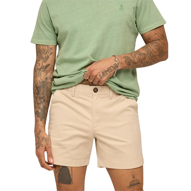 Man wearing a green shirt and beige shorts, showing tattoos on his arms.